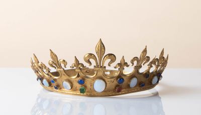 gold crown with blue and green stones on a white surface