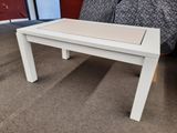 une table basse blanche avec un plateau blanc, posée sur un sol recouvert de moquette
