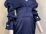 Le mannequin porte une robe bleue ornée de boutons dorés.