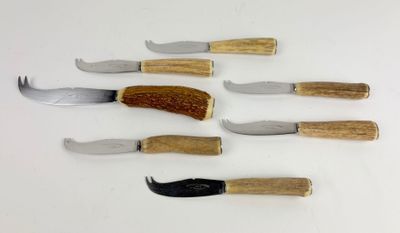 several knives and a fork are lined up on a white surface