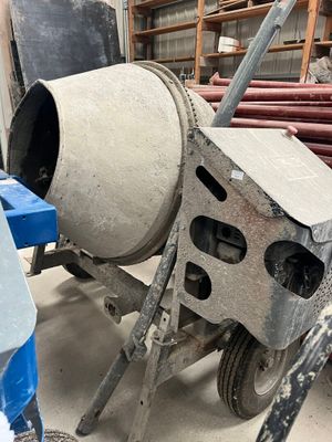 une bétonnière posée dans un garage, avec des outils par terre