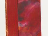 an old book with a red cover sitting on top of a white table