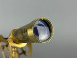an antique brass telescope with a blue glass lens on a gray background
