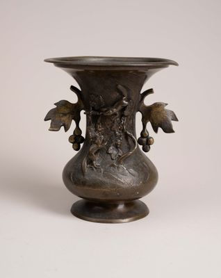 un vase en métal orné d'un oiseau, posé sur une surface blanche