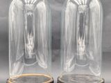 two clear glass bell jars with wooden bases on a grey background