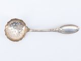 une cuillère ancienne en argent dont le manche repose sur une surface blanche