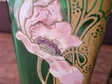 a green vase with a pink flower on it sitting on a table