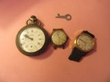 trois montres et une clé posées sur un fond rose