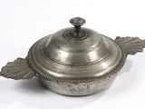 une casserole en argent avec un couvercle, posée sur une surface blanche