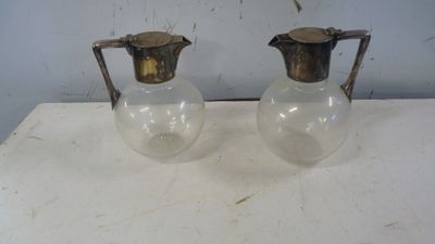 une paire de cruches anciennes en laiton et en verre posées sur une table blanche