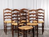 quatre chaises en bois sont alignées contre un rideau blanc