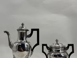 pair of silver plated teapots on stand on white background