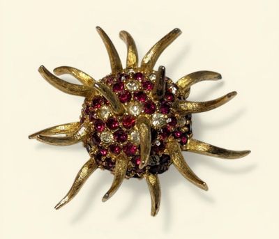 an image of a gold brooch with red and white stones on it
