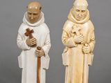two carved figurines of two men holding a cross and a dog