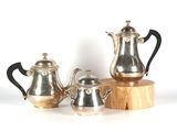 three silver teapots and a wooden stand on a white surface