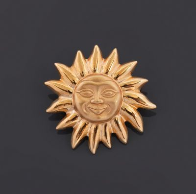 a close up of a gold sun broochle on a black surface