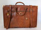 brown leather briefcase sitting on top of a white table next to a white wall