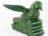 une statue d'oiseau vert posée au sommet d'une pile de livres