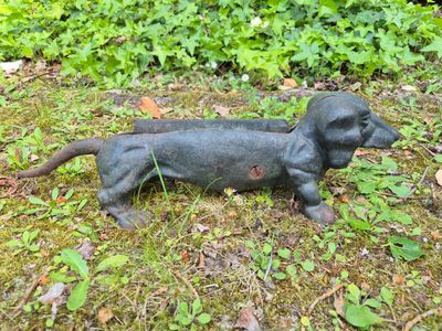 a statue of a dachshund laying in the grass