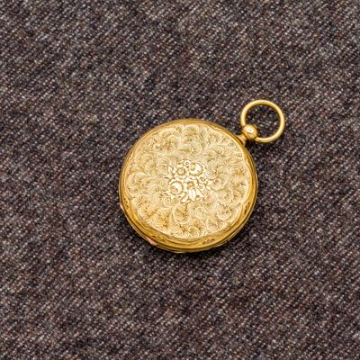 une image représentant une montre de poche en or posée sur un tissu marron
