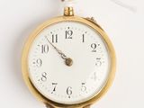 une montre à gousset en or suspendue à un mur blanc