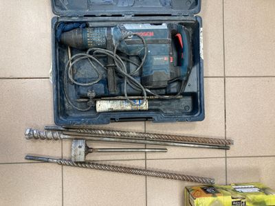 une boîte contenant un marteau, une perceuse et d'autres outils, posée par terre