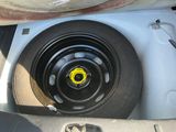 a tire with a yellow sticker on it in the trunk of a car
