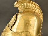 an antique gold helmet on a stand against a black background