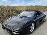 une voiture de sport noire garée sur le bord de la route, devant un champ