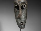 une image représentant un masque en bronze posé sur un socle en bois