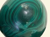 a green and black marble ball on a white surface