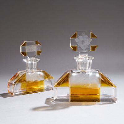 une paire de flacons de parfum en verre transparent et jaune posés sur une surface blanche