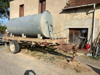 un grand réservoir monté sur une remorque, garé devant un bâtiment