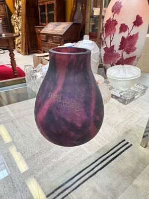 un vase violet posé sur une table dans une pièce où se trouvent d'autres vases