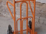 an orange hand truck with wheels in front of a brick wall