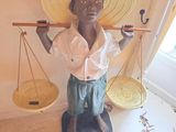 une statue représentant un garçon coiffé d'un chapeau de paille et tenant une balance