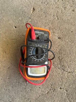 un multimètre orange et noir posé par terre, muni d'un cordon rouge