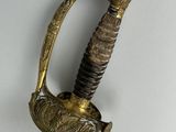 a gold colored sword with a black handle on a white surface