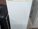 a small white refrigerator sitting next to a black chair
