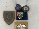 three medals and a wooden plaque on display on a white surface