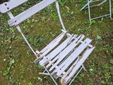 pair of white metal folding chairs sitting in the grass in front of a bush