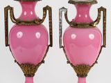 une paire de vases roses munis d'anses, posés sur des socles, sur fond blanc