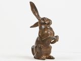 bronze sculpture of a rabbit holding a piece of wood in its paws