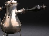 une cafetière en argent posée sur un support, sur fond noir
