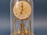 une horloge dorée sous un dôme en verre, sur fond bleu