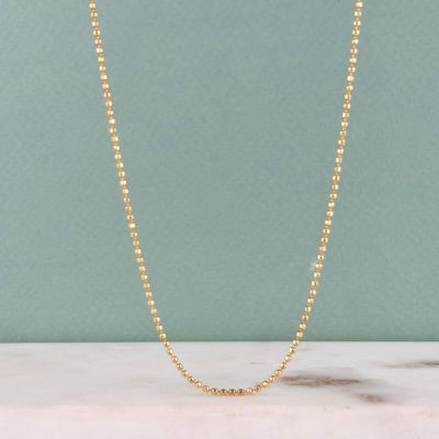 un gros plan d'un collier de perles dorées posé sur une surface en marbre