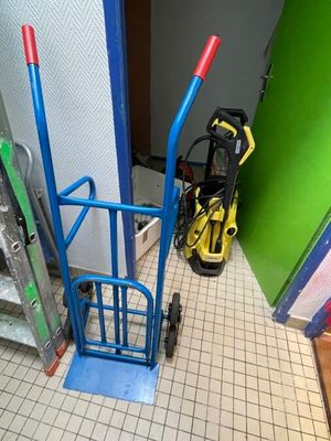 un diable bleu avec une poignée rouge à côté d'une porte verte