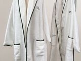 two white bathrobes hanging on a clothes rack next to a white wall