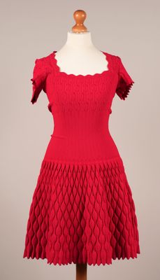 une robe rouge posée sur un socle de mannequin, avec un mannequin blanc
