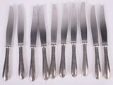 six silverplated knives are lined up on a white surface